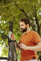 focado e ativo homem lubrificação e manutenção moderno bicicleta cadeia para anual verão manutenção. detalhado imagem mostrando caucasiano masculino habilmente lubrificante bicicleta pedais ao ar livre. foto