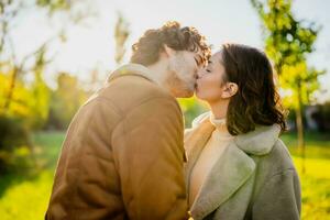 feliz amoroso casal se beijando dentro parque dentro pôr do sol. foto