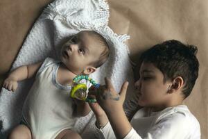 dois irmãos deitado e posando. retrato do irmãos. dois meses bebê Garoto e cinco anos pequeno Garoto jogando alegremente. Visão a partir de acima. emocional expressões do crianças. foto