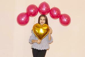 jovem lindo menina abraçando coração em forma dourado ar balão. dia dos namorados dia, aniversário, mulheres dia, aniversário, feriado celebração conceito foto