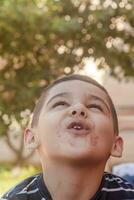 pequeno Garoto contorce-se dele face às ao ar livre. 6 anos velho criança dentro verão feriados. fofa pequeno Garoto enganar em volta. pessoas, infância estilo de vida conceito. retrato do jovem criança fazer engraçado rostos foto