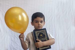 uma jovem meio Oriental Garoto com a piedosos alcorão. retrato do 5 anos velho muçulmano criança segurando uma piedosos Alcorão com branco fundo. livre espaço foto