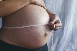 uma grávida mulher medindo dela barriga com uma fita foto