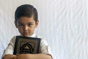 uma jovem meio Oriental Garoto com a piedosos alcorão. retrato do 5 anos velho muçulmano criança segurando uma piedosos Alcorão com branco fundo. livre espaço foto