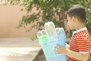 plástico poluição. pequeno Garoto coletado plástico garrafas e segurando reciclando bin. livre espaço foto