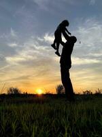 silhueta pai carregando filho contra céu durante pôr do sol foto