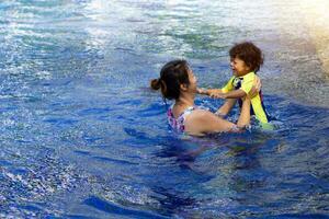 ásia criança Garoto aprender natação dentro uma natação piscina com mãe. - pôr do sol filtro efeito foto