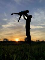 silhueta pai carregando filho contra céu durante pôr do sol foto