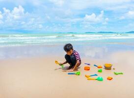 pequeno ásia Garoto jogar com areia em a de praia. foto
