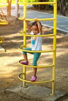 ásia menina é escalada em uma Parque infantil equipamento dentro uma escola. foto
