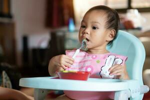 ásia bebê menina 11 meses ano velho é comendo Comida. foto