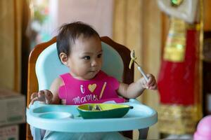 ásia bebê menina 11 meses ano velho é comendo Comida. foto