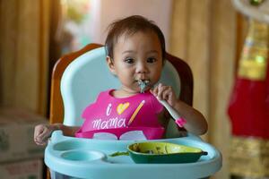 ásia bebê menina 11 meses ano velho é comendo Comida. foto