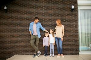 família com uma mãe, pai, filho e filha em pé de a parede do tijolo casa foto