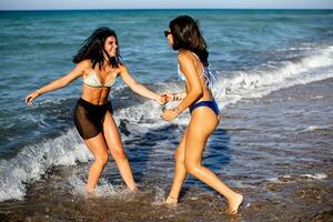 dois bonita jovem mulher tendo Diversão em a beira-mar foto