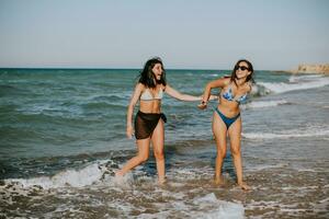 dois bonita jovem mulher tendo Diversão em a beira-mar foto