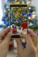 uma mulher fotografias decoração em Natal árvore com dele Smartphone foto