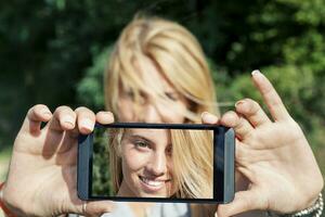 bonita mulher com loiro cabelo levar uma selfie com inteligente telefone foto
