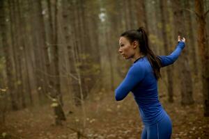 jovem com fato de treino azul alongamento antes do treino na floresta de outono foto