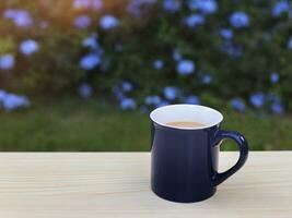 azul copo do café em a mesa dentro a jardim com roxa flores fundo. foto