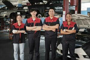 retrato do multirracial profissional mecânico equipe braços cruzado e Veja às Câmera, trabalhos às carro serviço garagem, feliz manutenção empregos, Verifica e reparar ocupação dentro automotivo indústria negócios. foto