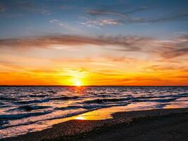 pôr do sol sobre a mar com ondas dentro a primeiro plano foto