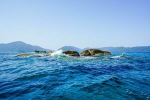 lindo marinha com espirrando ondas e rochoso litoral contra Claro azul céu. azul mar água superfície e rochoso costa. mergulho pontos dentro Tailândia surin ilhas. foto