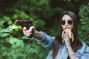 menina dentro a floresta aprende para tiro uma pistola enquanto comendo babanan foto