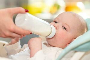mãe dá dela bebê leite a partir de uma garrafa às casa foto