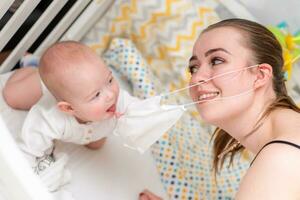 a bebê tentativas para lágrima fora a protetora mascarar a partir de dela mãe s face durante a coronovírus e covid-19 pandemia. foto