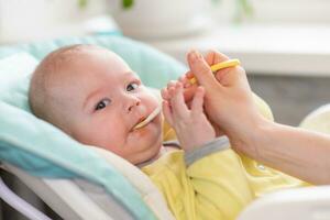 mãe feeds a bebê. a mãe coloca uma colher do amassado dentro a criança boca. a criança pequena come Comida. foto