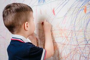 Garoto desenha em a parede com colori giz. a criança é acionado dentro criatividade às casa foto