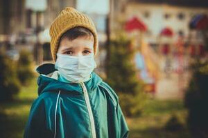 uma criança dentro uma médico mascarar carrinhos perto a Parque infantil durante a pandemia do coronavírus e cobiçado - 19 foto