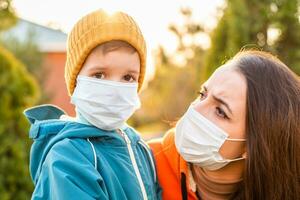 uma mãe e uma criança dentro médico máscaras andar em a rua durante a coronavírus e covid-19 pandemia. foto