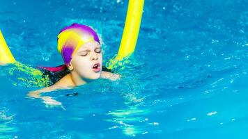 uma pequeno Garoto com uma vida Jaqueta em dele peito aprende para nadar dentro a interior piscina. foto