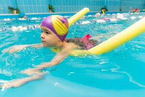 uma pequeno Garoto com uma vida Jaqueta em dele peito aprende para nadar dentro a interior piscina. foto