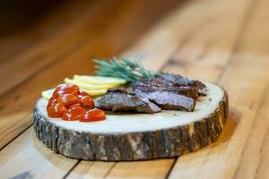 fatia de bife na tábua de madeira, decoração com rodela de limão, tomate e alecrim na mesa de madeira em ambiente de pouca luz. foto