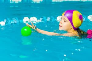 uma pequeno Garoto com uma vida Jaqueta em dele peito aprende para nadar dentro a interior piscina. foto