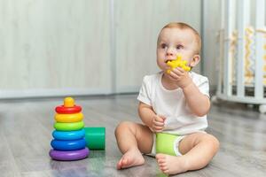 uma bebê é jogando em a chão. a Garoto é sentado em a chão. a criança leva a brinquedo para dentro dele boca e lambidas isto. foto