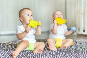 fofa feliz bebês jogar juntos em a chão com brinquedos e levar eles dentro seus bocas foto