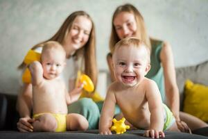 dois jovem mães estão jogando com seus feliz crianças dentro a quarto em a sofá. feliz bebê risos foto