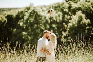 feliz e amoroso casal se beijando e jogando chapéu acima dentro verão foto