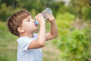 fofa criança bebidas água a partir de uma garrafa em a rua dentro verão foto