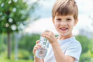 alegre criança bebidas Claro água a partir de uma garrafa em uma ensolarado dia dentro natureza foto