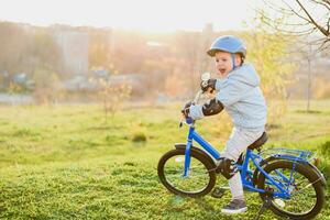 pequeno Garoto dentro capacete passeios uma bicicleta em uma ensolarado dia foto