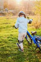 fofa criança é dirigindo uma bicicleta em uma ensolarado dia às pôr do sol foto