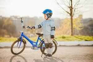 uma criança dentro uma capacete aprende para passeio uma bicicleta em uma ensolarado dia às pôr do sol foto