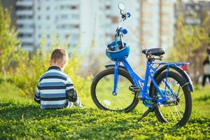 uma criança senta perto dele bicicleta às pôr do sol foto