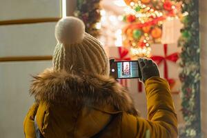 mulher turista leva fotografias do festivo cidade decoração em dela Smartphone. foto