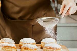 chef de mulher prepara rosquinhas frescas em sua padaria. cozinhar sufganiyot de hanukkah judaico tradicional. conceito de empresa de pequeno porte. foto